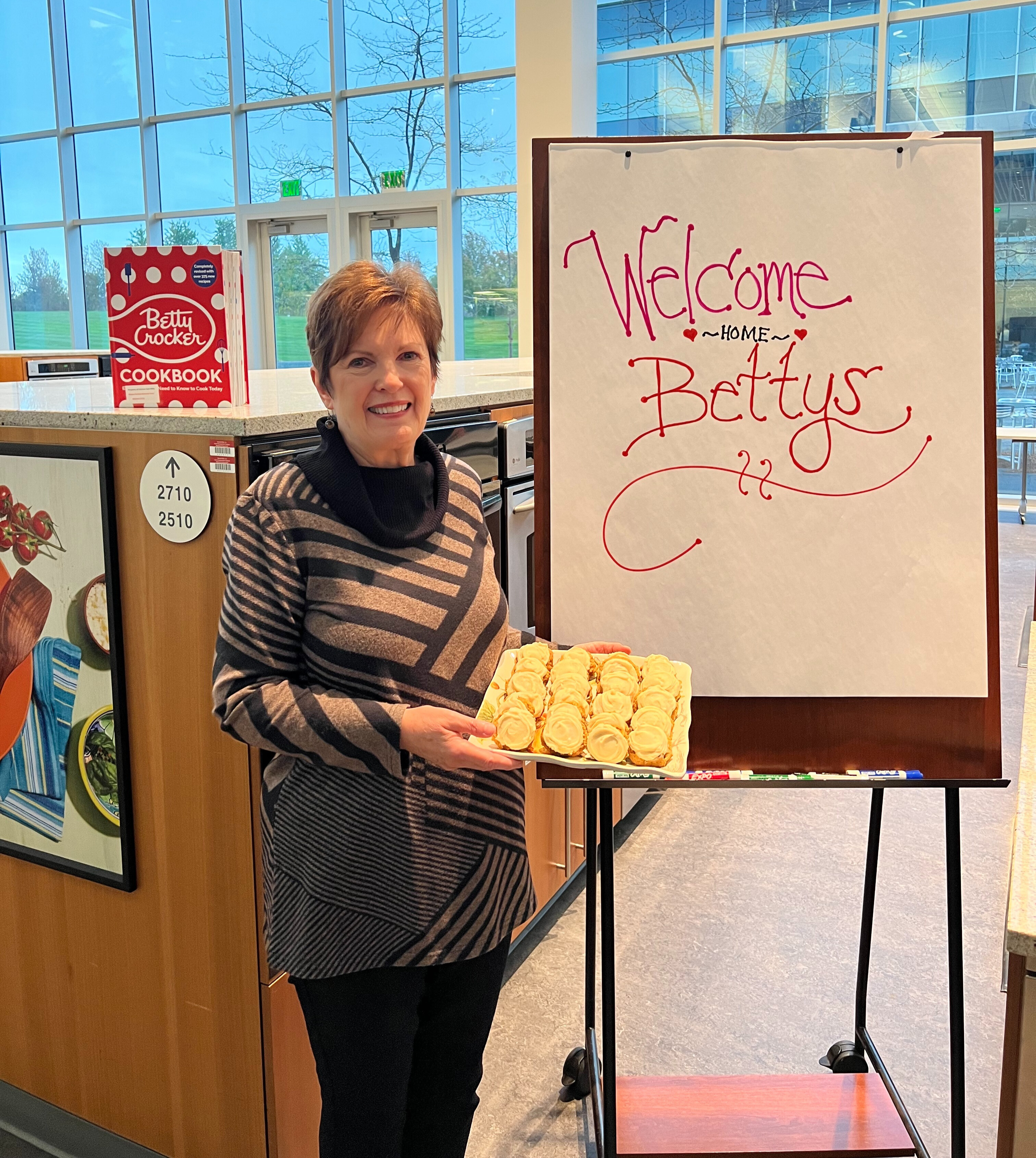 Jackie Sheehan posing with her Spiced Pumpkin Cookies in front of a sign that says “Welcome Home Bettys”