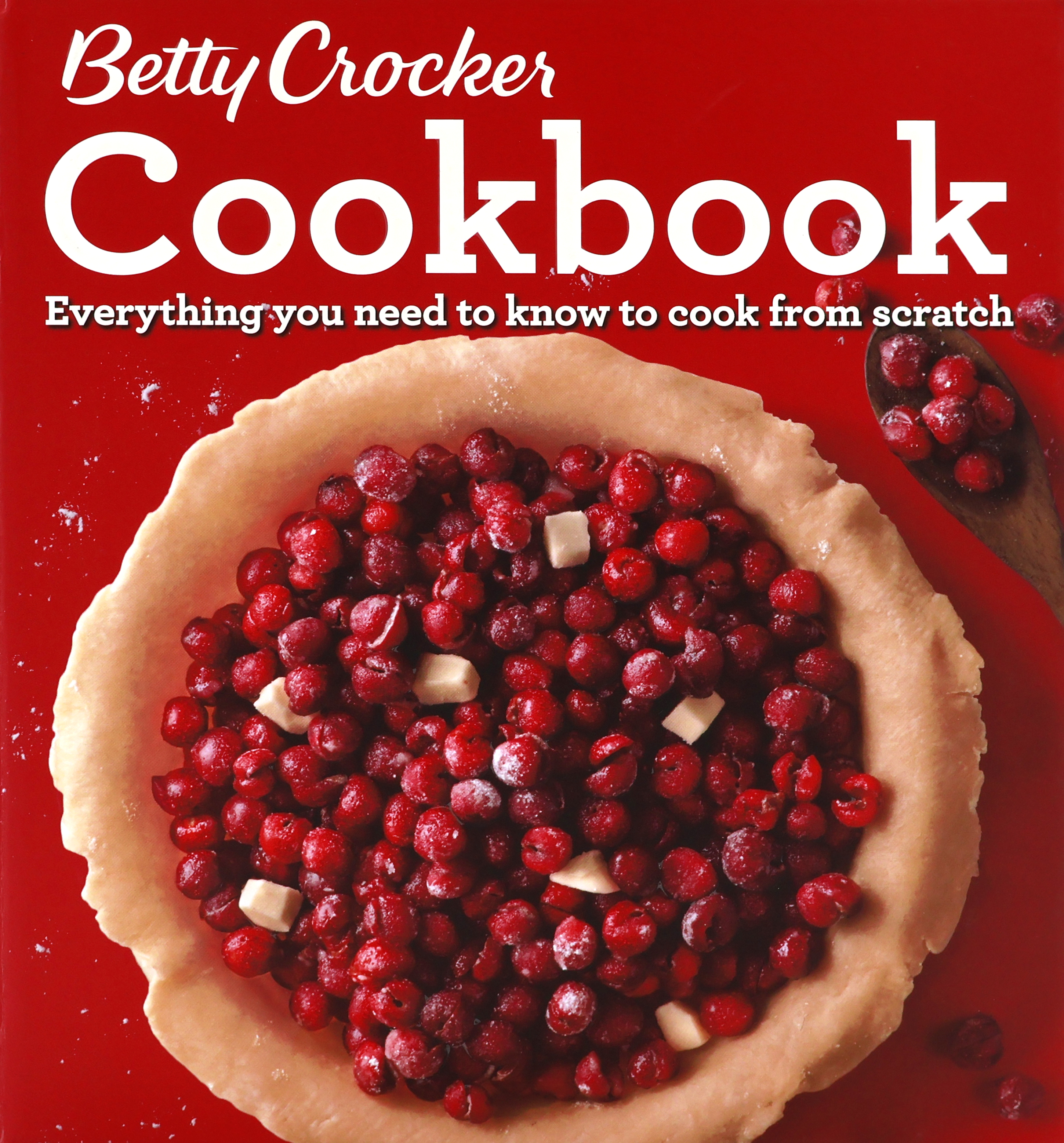 Cover of the 2016 Betty Crocker Cookbook with a red cover that has a photo of an unbaked open-face one-crust cherry pie.  The cherries on the pie are raised/embossed. There is a wooden spoon with cherries lying next to the pie.  “Everything you need to know to cook from scratch” is written in white under the large “Cookbook” word this is also white.